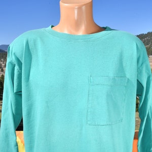 May include: A turquoise long-sleeved t-shirt with a single pocket on the left side.