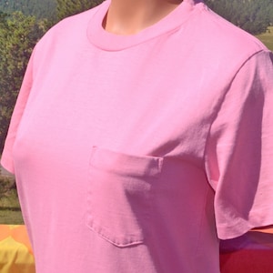 May include: A plain pink t-shirt with a single pocket on the left side.