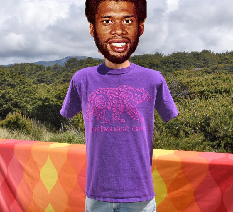 Puede incluir: Camiseta morada con cuello redondo, con un dise&ntilde;o de oso rosa y el texto "Northwest Tree". La camiseta de manga corta est&aacute; hecha de un material suave. El fondo muestra un paisaje verde y una tela colorida.