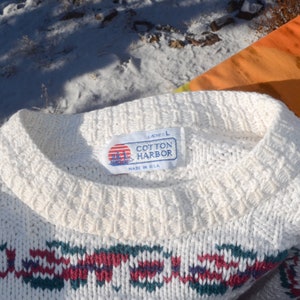 May include: White cotton sweater with a red, green, and blue geometric pattern. The sweater has a crew neck and a label that reads "Ladies L Cotton Harbor Made in USA."