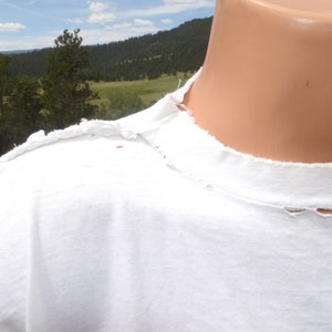 Op de afbeelding: Wit T-shirt met een distressed, rafelige halslijn. Het shirt heeft een paar kleine gaatjes in de stof.