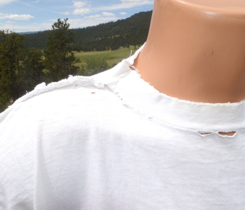 Op de afbeelding: Wit T-shirt met een distressed, rafelige halslijn. Het shirt heeft een paar kleine gaatjes in de stof.