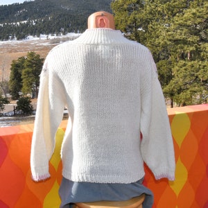 May include: White knitted sweater with a mock neck and long sleeves. The sweater has a subtle textured pattern and a slightly cropped length.