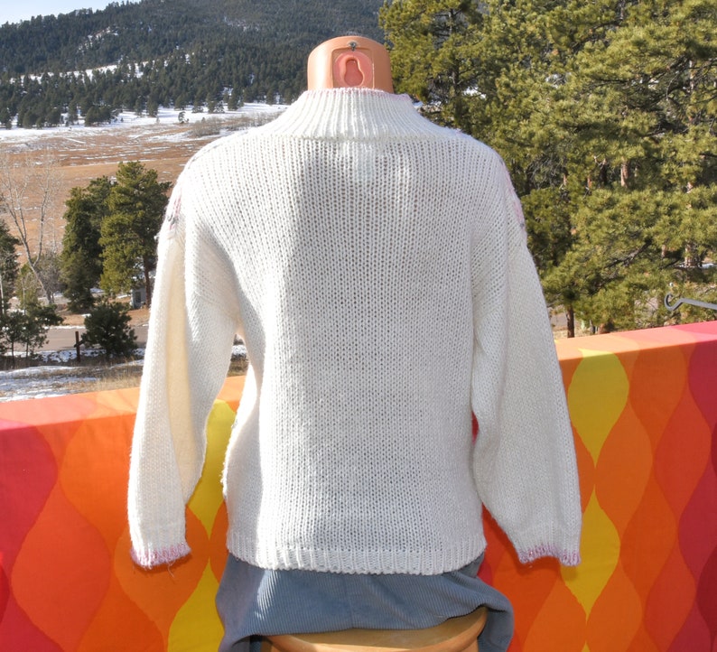 May include: White knitted sweater with a mock neck and long sleeves. The sweater has a subtle textured pattern and a slightly cropped length.
