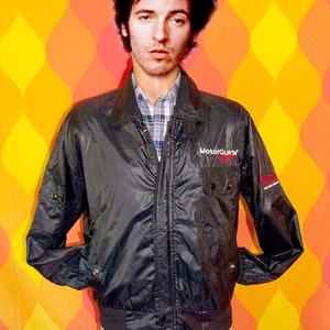 May include: A black nylon jacket with a zipper closure and a red and white "MotorGuide" logo on the left chest. The jacket has two pockets on the front and a red and white "MotorGuide" logo on the right sleeve.