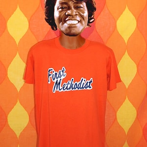 May include: An orange t-shirt with the text "First Methodist" in blue lettering.