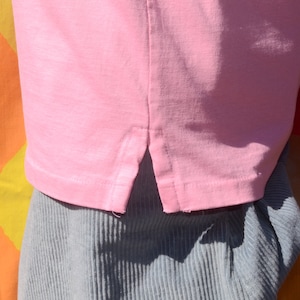 May include: A pink t-shirt with a side slit detail. The shirt is made of a soft, lightweight fabric.