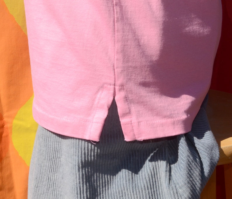 May include: A pink t-shirt with a side slit detail. The shirt is made of a soft, lightweight fabric.