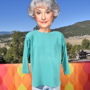 May include: A turquoise long-sleeved t-shirt with a single pocket on the left side.