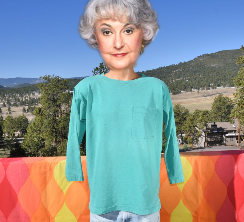 May include: A turquoise long-sleeved t-shirt with a single pocket on the left side.