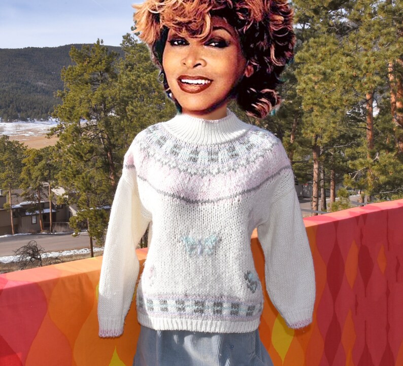 May include: White knitted sweater with a pink, gray, and blue geometric pattern. The sweater has a mock neck and long sleeves.
