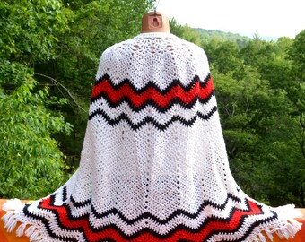 May include: White crochet throw blanket with black and red zigzag stripes and fringe trim.