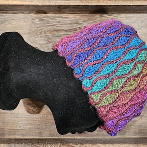 May include: A colorful crocheted hat with a wavy pattern in shades of purple, blue, green, and brown. The hat is displayed on a black mannequin head.