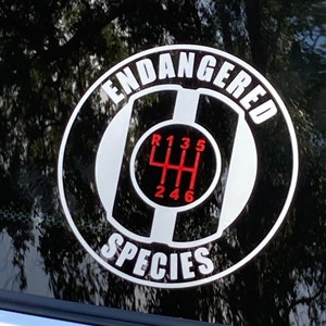 May include: A black and white sticker with the words "Endangered Species" around a stylized gear shift pattern. The gear shift pattern is in red and white.