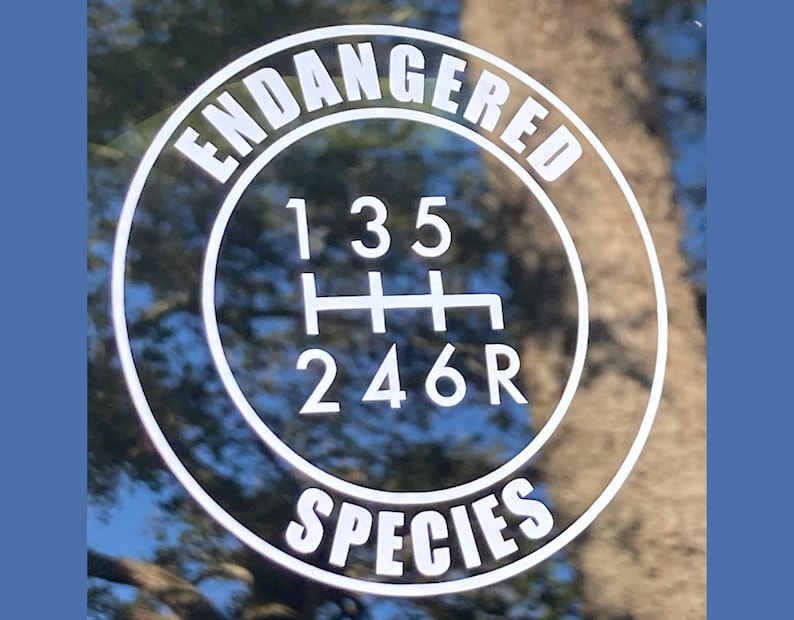 May include: A black and white sticker with the text "Endangered Species" in a circle around a gear shift pattern with the numbers 1, 3, 5, 2, 4, 6, and R.