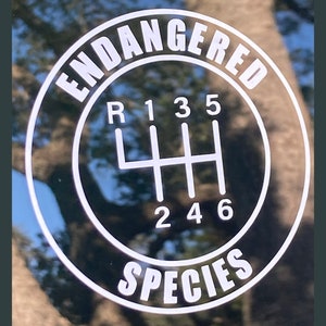 May include: A black and white sticker with the text "Endangered Species" in a circle around a white gear shift pattern with numbers 1, 2, 3, 4, 5, and 6.