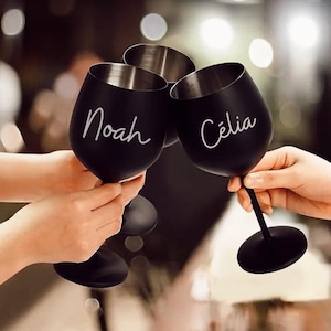 Puede incluir: Tres copas de vino negras con letras blancas. Las copas están etiquetadas con "Noah", "Celia" y una tercera copa con letras ilegibles.