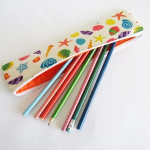 May include: A beige pencil case with a zip, decorated with colourful seashell and starfish patterns. The case is open, revealing several coloured pencils in shades of blue, red, and green.