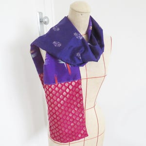 May include: A purple and pink silk scarf with a geometric pattern. The scarf is folded and draped around a dress form.