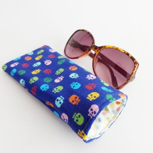 May include: A blue fabric sunglasses case with a colourful skull pattern. The case is rolled up and has a white polka dot lining.