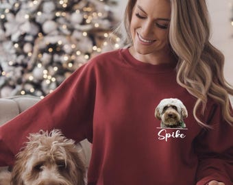 May include: A maroon sweatshirt featuring a dog portrait and the name "Spike" in white script. The sweatshirt is worn by a person sitting on a couch with a dog. A Christmas tree is in the background.