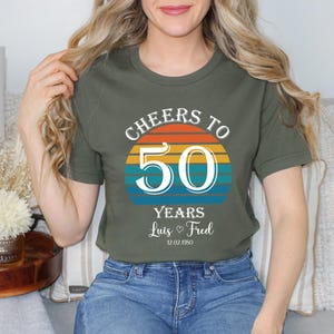 May include: A green t-shirt with a sunset graphic and the text "Cheers to 50 Years Luis & Fred 12.02.1950".