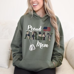 May include: Green hooded sweatshirt with the text "Proud Army Mom" in white lettering. The text "Army" is in a camouflage pattern. A small American flag is above the text. Two silver dog tags hang from the text "Army".