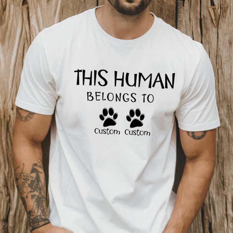 May include: White t-shirt with the text "This Human Belongs To" and two paw prints with the word "Custom" under each paw print.