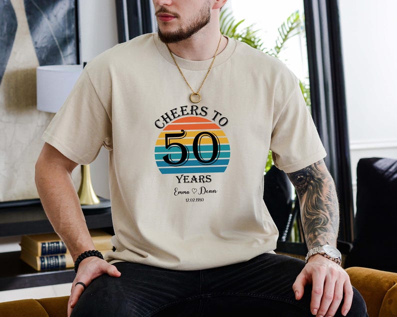 May include: A beige t-shirt with a retro sunset graphic and the text "Cheers to 50 Years Emma &hearts; Dean 12.02.1950".