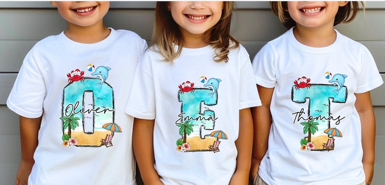 May include: Three white t-shirts with a blue watercolor letter, a crab, a dolphin, a beach scene, and a palm tree. The letters are O, E, and T. The names Oliver, Emma, and Thomas are written below the letters.