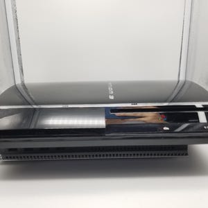 May include: A black PlayStation 3 games console featuring a glossy finish, a disc slot on the front, and the text PlayStation 3 printed on the top surface. The device has a rectangular shape with a vented base and a power button on the front panel.