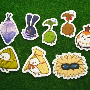 Puede incluir: Un conjunto de nueve pegatinas coloridas con varios personajes de dibujos animados. Las pegatinas están impresas en papel blanco y tienen un acabado brillante. Los personajes incluyen un cristal morado, un conejo negro, una planta verde, un hongo marrón, un pájaro naranja, un pastel de arroz verde, un pájaro amarillo, una flor amarilla y un monstruo de ojos azules.