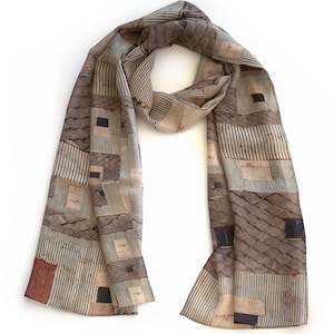 May include: A rectangular scarf with a repeating pattern of squares, rectangles, and vertical stripes in shades of brown, beige, and black. The scarf is draped and appears to be made of a lightweight fabric.