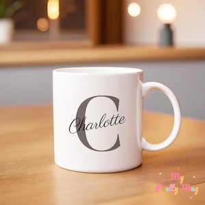Peut inclure: Une tasse en céramique blanche avec une grande lettre "C" grise et le nom "Charlotte" écrit en cursive noire en dessous.