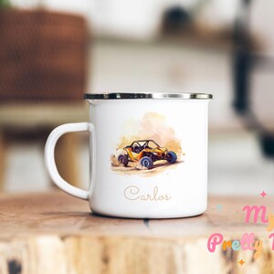 Puede incluir: Taza de esmalte blanco con borde y asa negros. La taza presenta una ilustración de acuarela de un buggy de dunas amarillo y naranja con ruedas azules. El nombre "Carlos" está escrito en cursiva dorada debajo.