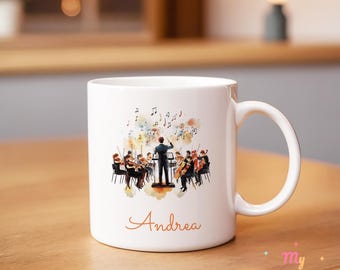 Op de afbeelding: Witte keramische mok met een aquarel illustratie van een orkest, inclusief dirigent en muzikanten. De naam "Andrea" is in cursief geschreven. De mok heeft een gebogen handvat.