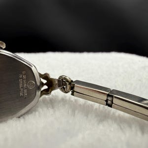 May include: Close-up of a vintage silver-toned wristwatch. The watch face is oval-shaped with a silver band. The watch has a decorative design on the top and the back of the watch has text that reads "D. Gruen Watch Co. ST. STEEL BACK."