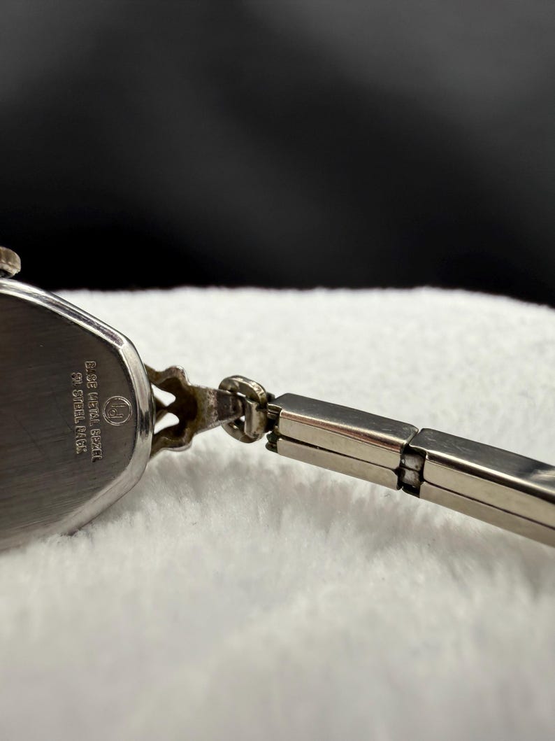 May include: Close-up of a vintage silver-toned wristwatch. The watch face is oval-shaped with a silver band. The watch has a decorative design on the top and the back of the watch has text that reads "D. Gruen Watch Co. ST. STEEL BACK."