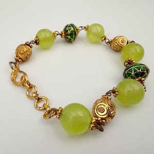 May include: A bracelet featuring round, translucent light green beads alternating with textured gold-tone metal beads and smaller, dark green and gold enamel-accented beads. The piece is connected by gold-tone metal links and a circular clasp.