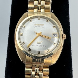 May include: A gold-tone Longines Ultra-Chron automatic wristwatch with a silver dial, gold hands, and gold hour markers. The watch features a date window at the three o'clock position and a gold-tone metal link bracelet with a secure clasp.