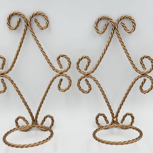 May include: Two gold metal wall mounted plant holders with a decorative twisted rope design. Each holder has a circular base for a small plant pot.