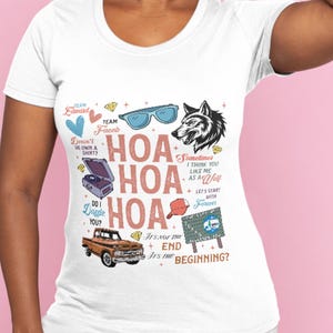 May include: White t-shirt with a variety of graphics and text. The design includes a wolf, sunglasses, a record player, a truck, and the words "HOA" repeated three times. Other text includes "Team Edward," "Team Jacob," and "It's not the end, it's the beginning?"