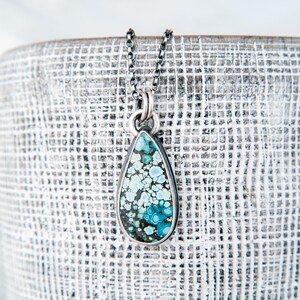 May include: A teardrop-shaped pendant necklace featuring a polished turquoise stone with intricate dark matrix patterns. The stone is set in a smooth silver bezel and hangs from a delicate, dark oxidized silver chain with small round links.