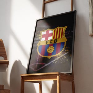 May include: A framed print of the FC Barcelona logo with a black background and yellow, red, and blue accents. The logo is surrounded by a splatter of white paint.