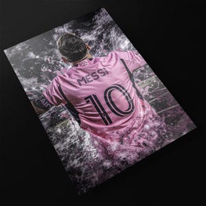 May include: A pink soccer jersey with the name "Messi" and the number "10" printed on the back. The jersey is surrounded by a white and gray abstract design.