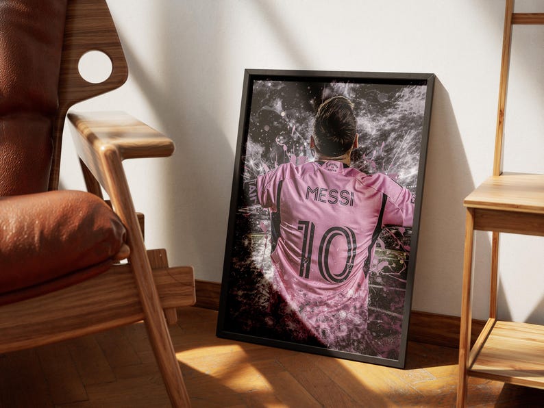 May include: A black framed poster with a pink and black image of a soccer player wearing a pink jersey with the number 10 and the name "Messi" on the back. The player is surrounded by a white and gray abstract design.