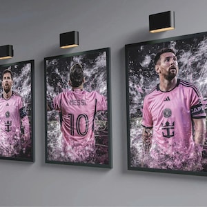 May include: Three framed images of a soccer player wearing a pink jersey with black accents. The jersey has the number 10 and the text "Messi" on the back. The player is wearing a captain's armband with the text "Captain" on it. The jersey also has a logo with a crown and the text "Inter Miami CF".