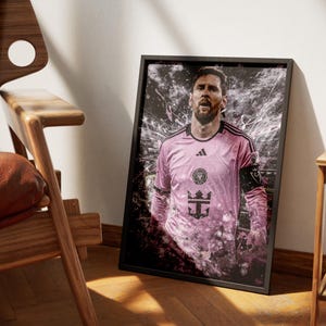 May include: A black and white photo of a soccer player wearing a pink jersey with a black and white logo. The player is standing in front of a blurred background with a white and black design.