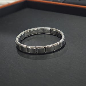 May include: A silver bracelet made of interlocking links. The bracelet is made of metal and has a polished finish.