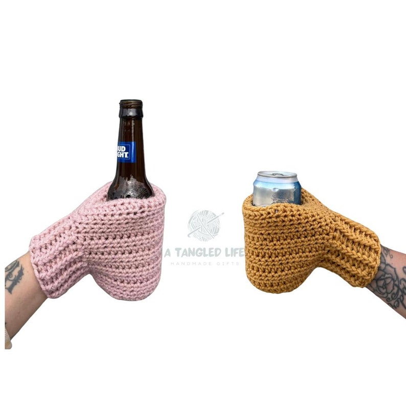 Pode incluir: Dois porta-bebidas de croch&ecirc;, um rosa e outro amarelo mostarda, segurando uma garrafa de cerveja e uma lata de cerveja. Os porta-bebidas t&ecirc;m a forma de uma m&atilde;o com um polegar e quatro dedos.